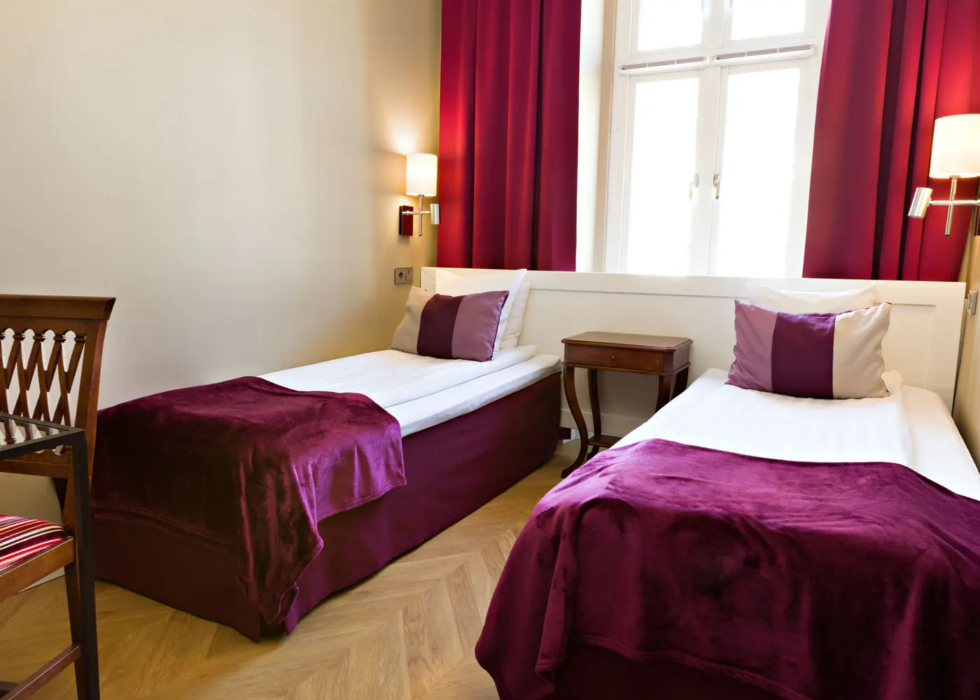 Tvåbäddsrum på Hotel Vasa med vinröda textilier och höga fönster